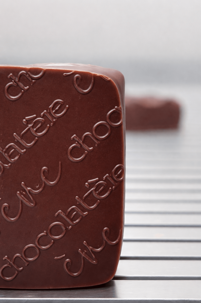 Praline aus zartschmelzender dunkler Schokolade, mit glänzend glatter Oberfläche und eingeprägtem Schriftzug eve chocolatiere Tübingen